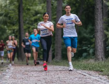 smiling racers running through the woods along a gravel path 